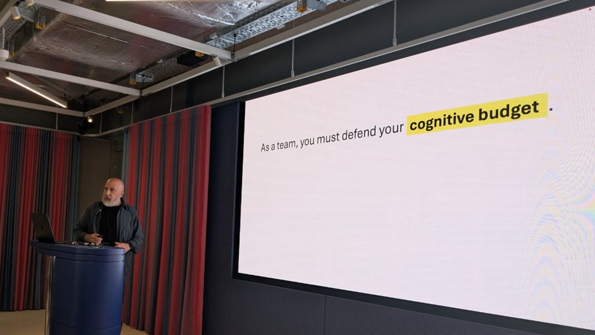 Giuseppe presenting a slide that says: As a team, you must defend your cognitive budget.