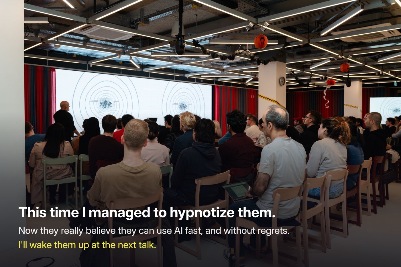 The room at buildersklub from the back, everyone watching the loop's spiral on the big screens. On it: This time I managed to hypnotize them. Now they really believe they can use AI fast, and without regrets. I'll wake them up at the next talk.
